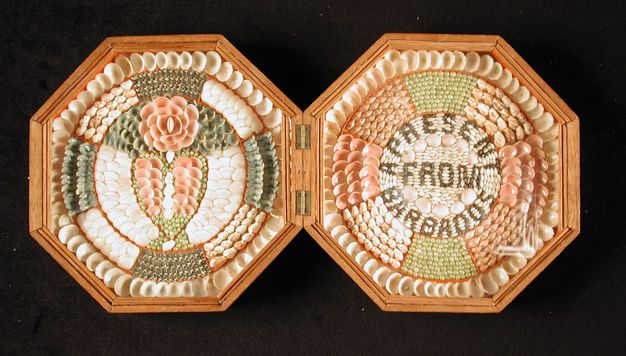 A double-sided sailor’s valentine, hinged at the centre, displaying symmetrical shell patterns with a heart motif on one side and the words 'a present from Barbados' spelled in shells on the other.